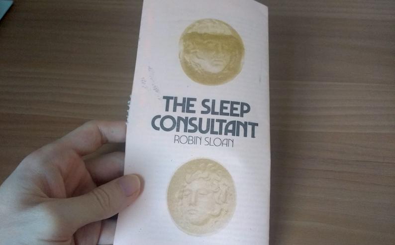 Adam Westbrook holding a copy of “The Sleep Consultant” by Robin Sloan